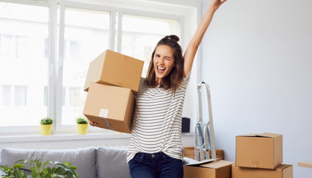 Joyful young woman standing in new apartment with arm raised after moving in