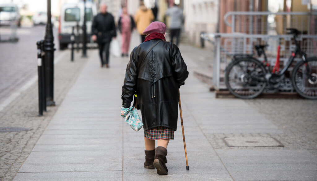 Starsza kobieta z laską, spacerująca po ulicy