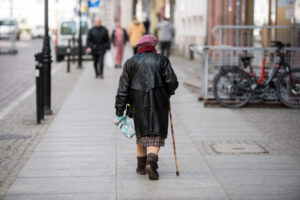 Starsza kobieta z laską, spacerująca po ulicy