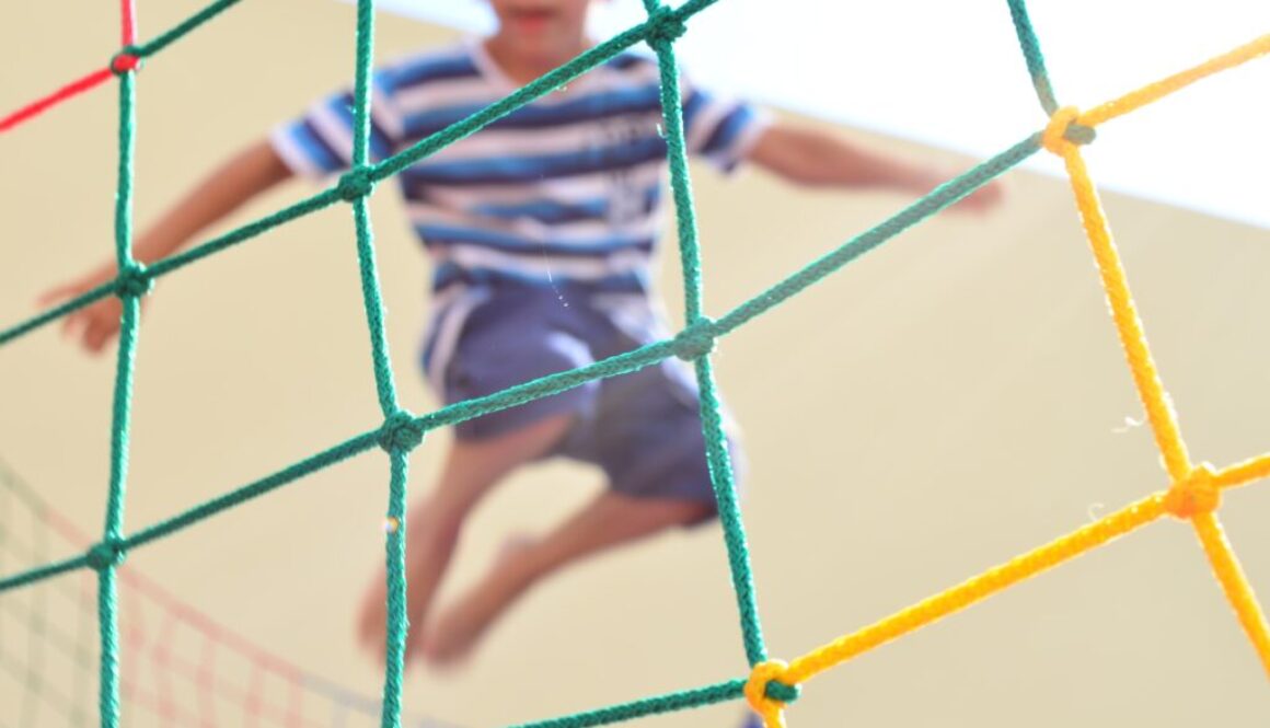 Chłopiec skaczący na trampolinie, ogrodzonej kolorową siatką