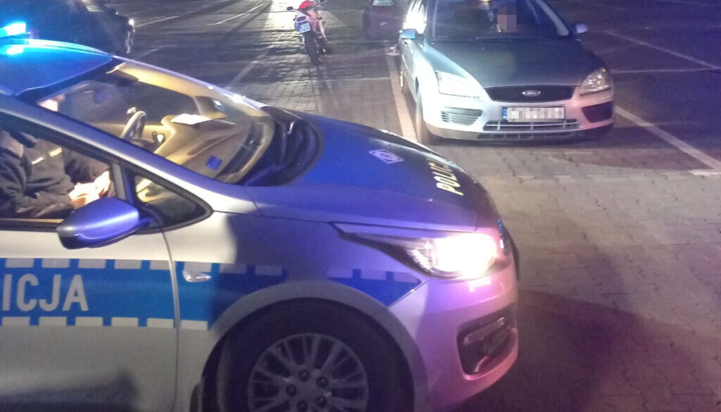 Samochód policyjny w nocy na parkingu kontroluje kierowcę osobówki