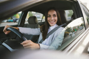 Beautiful happy successful businesswoman is driving a new modern car in good mood. Portrait cute female driver steering car with safety belt